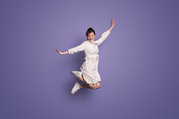 Fototapeta na wymiar Full length body size photo of pretty screaming girl wearing dress while jumping isolated over purple background. Happy people positive emotion. Positive person