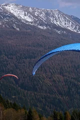 Fotobehang A shot of Two men in paragliders flying in the mountains Winter  forest in Trentino-Alto Adige Italy © Adela_dg/Wirestock Creators