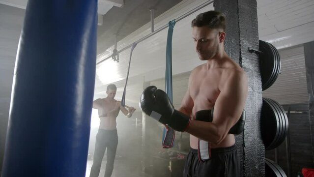 Male fighter wearing boxing gloves to fight while another man practicing karate with nunchuck at the gym. Slow-motion shot