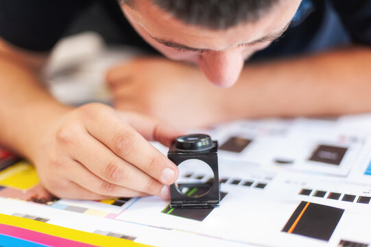 Young man in the process of printing used color scales and loupe and management color correction. Spectrophotometer, print measuring.