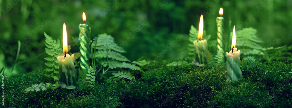 Sticker burning candles on moss, dark green blurred natural background. magic candles for witch ritual in fo