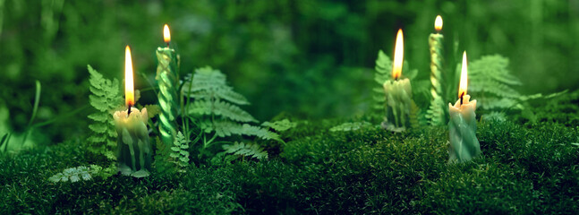 burning candles on moss, dark green blurred natural background. magic candles for witch ritual in...