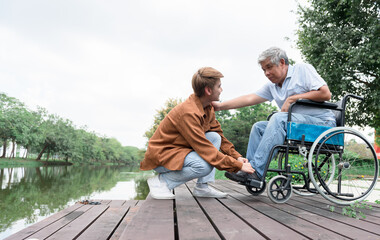 Asian family, The son is taking care of his father by tying his shoelaces for him. who is sitting in a wheelchair with love and care. to relationship in family and retirement age health care concept.