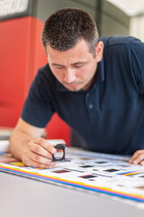 Young man in the process of printing used color scales and loupe and management color correction....