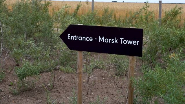Wooden sign of the entrance to the Marsk Tower, surrounded by green plants swaying in the wind