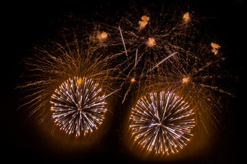 beige and yellow fireworks burst into various shapes in the sky during the holiday