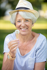 happy elderly woman senior sitting on grass blowing on dandelion