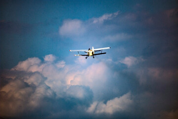 A light plane with a propeller in front flies in the blue sky among the clouds