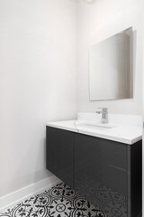 A modern bathroom with a dark grey vanity cabinet, a black and white pattern tile floor, and a chrome faucet on a white marble countertop.