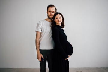 young couple family a man in a white T-shirt with a beard hugs his wife a pregnant woman with a big belly in a black dress, look into the frame

