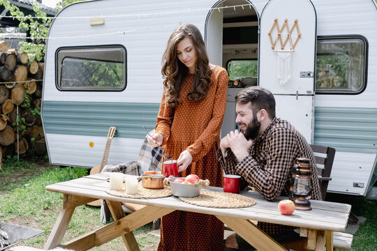 Young caucasian couple is traveling in van. Romantic atmosphere of relaxation. Road trip around country for the weekend. Happy loving man and woman preparing mulled wine near the camper