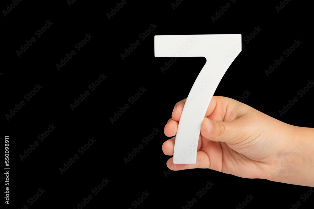Poster number seven in hand isolated on black background. number 7 in a child's hand on a black background.