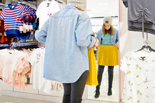 Young woman holding skirt in front of mirror while shopping at store