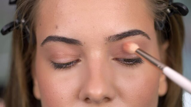 Close up of young woman's eyes and make up artist hand, applying nude eyeshadow. 