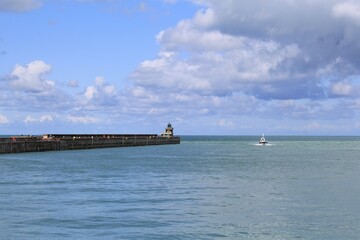 a seascape at the french coast in september with the pier and a little boat in the sea and a blue sky with clouds