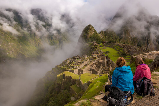 Two young women looking over ruins high in the mountains. Machu Picchu, Peru.