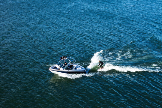 A happy athletic man wake surfs behind his wakeboard boat in Idaho.