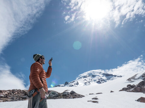 A man takes a picture with his phone in while hiking on Mount Baker, Washington.