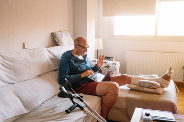 Obraz premium Injured man with bandaged foot using a laptop.