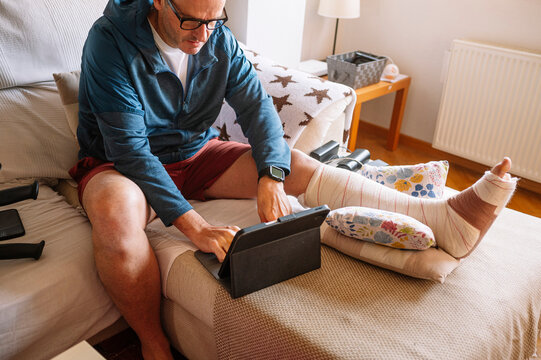 Injured man with bandaged foot using a tablet.