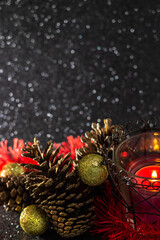 Fototapeta na wymiar Decoração natalina. Uma vela acesa com bolas douradas, festão e pinhas com um fundo preto brilhante.