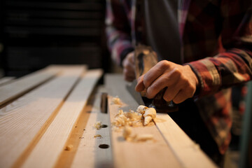 Curled wood shavings are created as a carpenter uses a hand planer to work on a piece of wood.