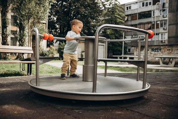 a child of 2-3 years old walks on the playground and spins on the carousel