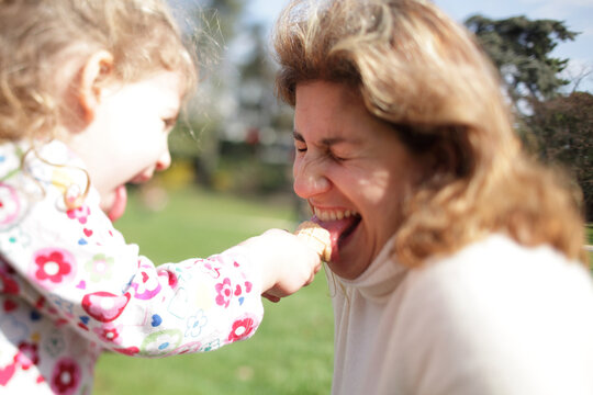 A two year-old girl laughs with her mother while sharing her ice cream cone, Paris, France