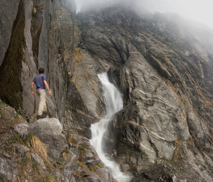 A young man stands besides a large waterfall in the Modi Khola valley, Annapurna Himalaya, Nepal.