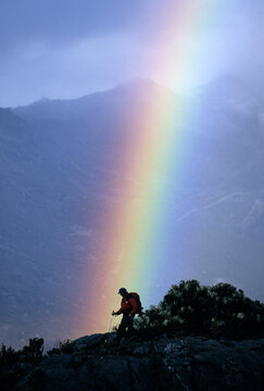 A hiker passes below a rainbow.