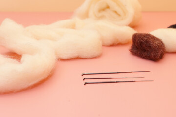 needle felting kit with white wool on pink table. small woolen handmade product with skeins of wool
