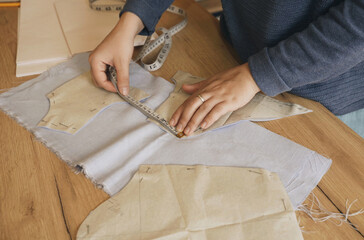 Fashion designer woman measures cut paper patterns in workshop.