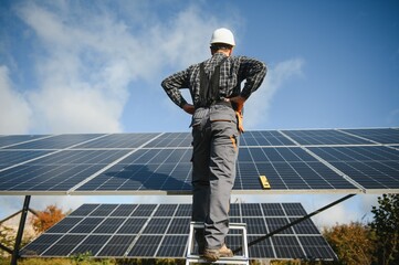 Male worker in uniform outdoors with solar batteries at sunny day.