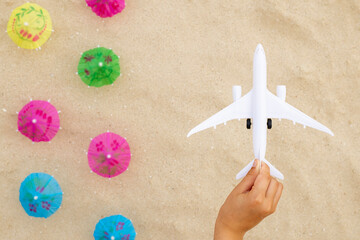 Childs hand with toy airplane under over sandy beach with beach umbrellas