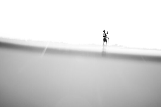 Black and white low angle split level image of one man paddling a stand up paddleboarding (SUP) against a blown out sky.