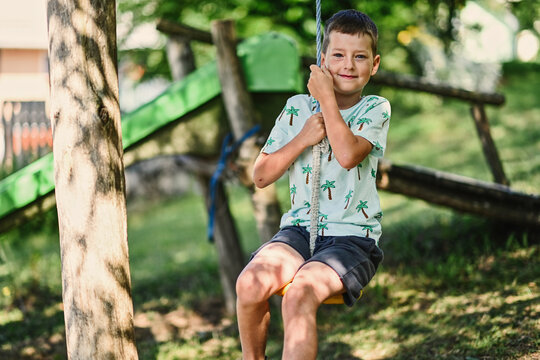 Boy swinging on a rope against slide in mountain village.