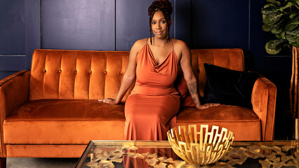 Black woman in orange dress sitting on orange couch