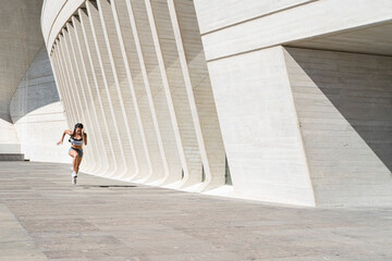 Pulled back view of female athlete running on concrete