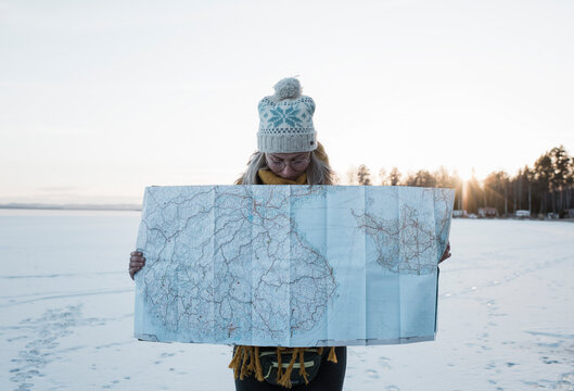 woman holding a large map whilst standing on a frozen lake in Sweden