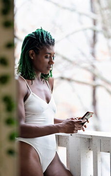 Black woman with green dreadlocks on the patio holding cell phone