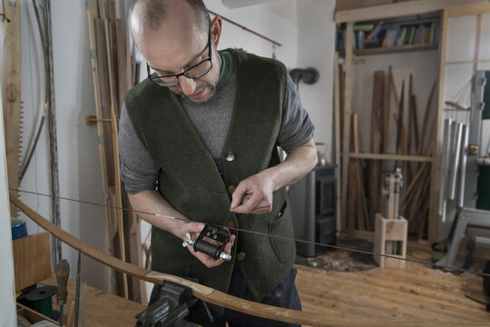 Male bow maker adjusting bow string in workshop, Bavaria, Germany