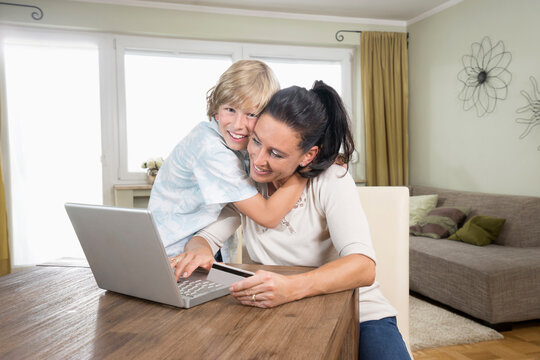 Boy hugging his mother while she online shopping on laptop, Bavaria, Germany
