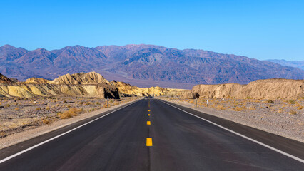 Fototapeta na wymiar Desert Road - A wide angle view of newly resurfaced highway 190, extending towards rugged purple Panamint Range, at side of Zabriskie Point on a sunny Winter day, Death Valley National Park, CA, USA.