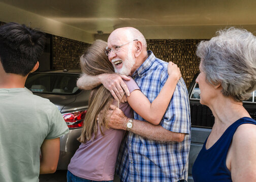 Smiling grandfather hugs teen granddaughter as grandmother looks on.