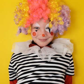 A boy in a clown costume on the background of a bright yellow wall is fooling around and smiling