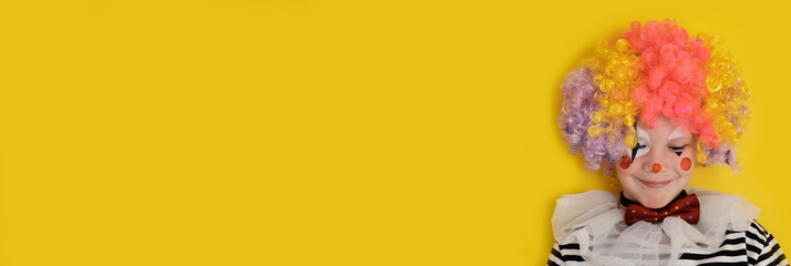 A boy in a clown costume on the background of a bright yellow wall is fooling around and smiling