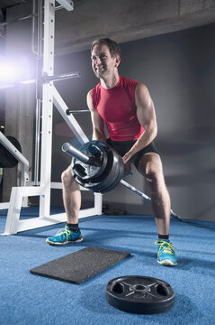 Mid adult man doing bent over row exercising with long barbell in the gym, Bavaria, Germany