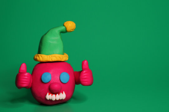 A virus figurine in a festive hat with thumbs up. Green background. Christmas toys.