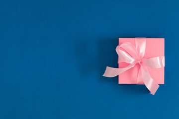 Pink gift box with pink bow on dark blue background. Valentine day, 8th march, Mothers day background. Flat lay, top view, copy space