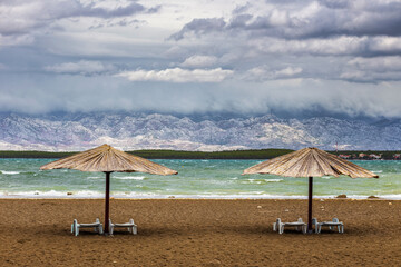 Nin, Croatia - Two reed sunshades at the empty Queen's Beach by the mediterranean town of Nin at the end of summer with Velebit Mountains at background and turquoise Adriatic sea water at autumn time